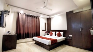A hotel room with a bed, a wardrobe, a bedside table, a ceiling fan, and a curtain. - Hotel Paradise Inn (New Delhi)