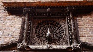A detailed carved wooden door with a peacock design, set in a brick wall. - Unique Guest House (Bhaktapur)