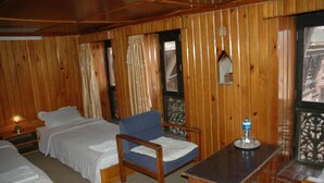 A wooden-paneled room with two beds, a chair, a table, and a window with a view. - Unique Guest House (Bhaktapur)
