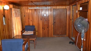 A room with wooden walls, a table, two chairs, a fan, and a door. - Unique Guest House (Bhaktapur)