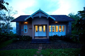 A two-story house with a stone facade, a tiled roof, and a front porch. - After the Rains (Vythiri)