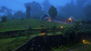Una casa tradicional con techo inclinado, rodeada de exuberante follaje y muros de piedra.