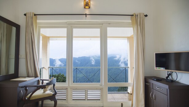 Una habitación con un ventanal grande, una silla, un escritorio, un televisor y un armario.