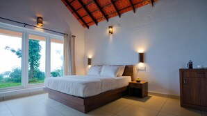 Un dormitorio con una cama grande, dos lámparas de noche, una mesita de noche y vistas al exterior con vegetación.