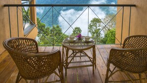 Un balcón con sillas de mimbre, una mesa y vistas a un paisaje montañoso.