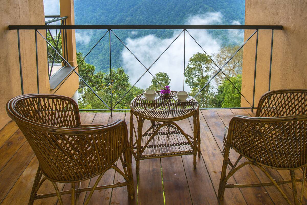A balcony with wicker chairs, a table, and a view of a mountainous landscape.