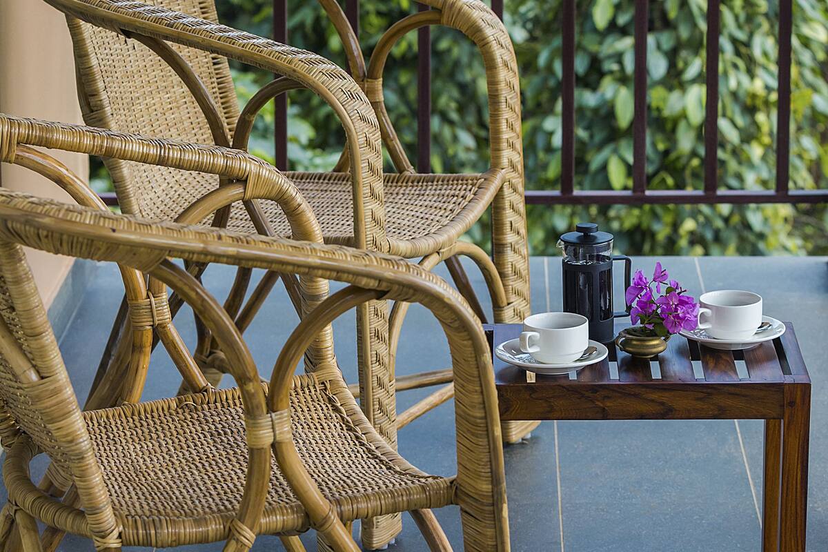 A wicker chair and table set on a balcony with a view of greenery.