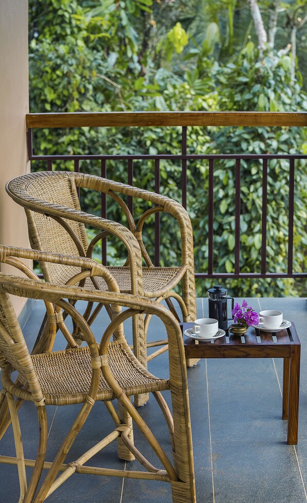 Un ensemble de chaise et de table en osier, placé sur un balcon offrant une vue sur la verdure.