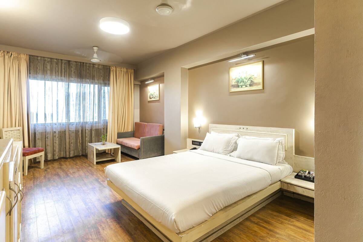 Habitación de hotel con una cama grande, un escritorio, una silla y una ventana con cortinas.