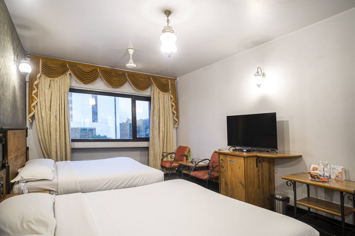 Habitación de hotel con dos camas, televisión, escritorio con silla y ventana con cortinas.