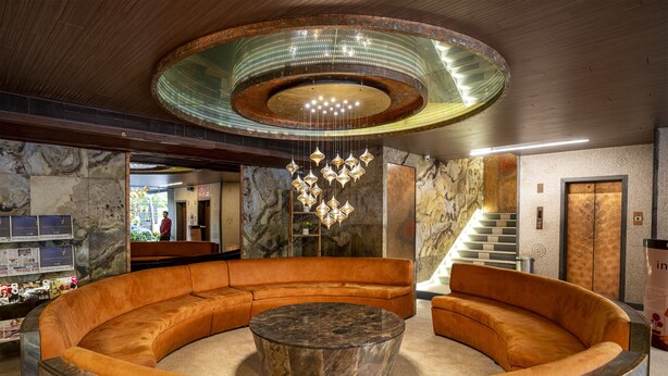 A circular seating area with a central marble table, a modern chandelier, and a marble wall with a staircase. - Infiniti Hotel & Spa (Indore)