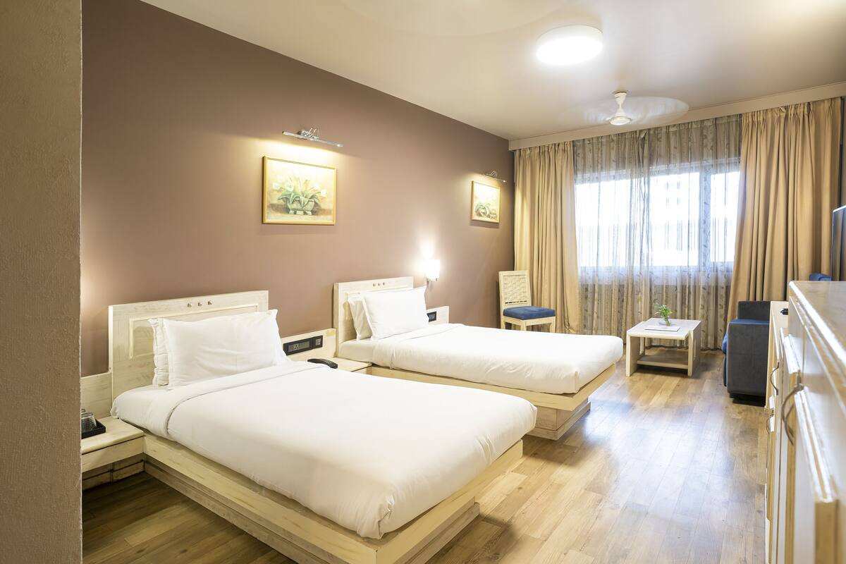 Una habitación de hotel con dos camas, una mesita, una silla y un televisor.