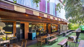 An outdoor dining area with wooden tables and chairs, a blue cooler, and a green artificial turf floor. - Infiniti Hotel & Spa (Indore)