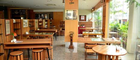 Un restaurante con mesas y taburetes de madera, un reloj en la pared y vistas al exterior a través de amplias ventanas.