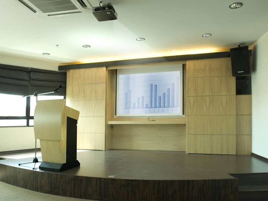 Un salón de conferencias con un atril, una gran pantalla de proyección que muestra un gráfico de barras y un revestimiento de pared de madera.