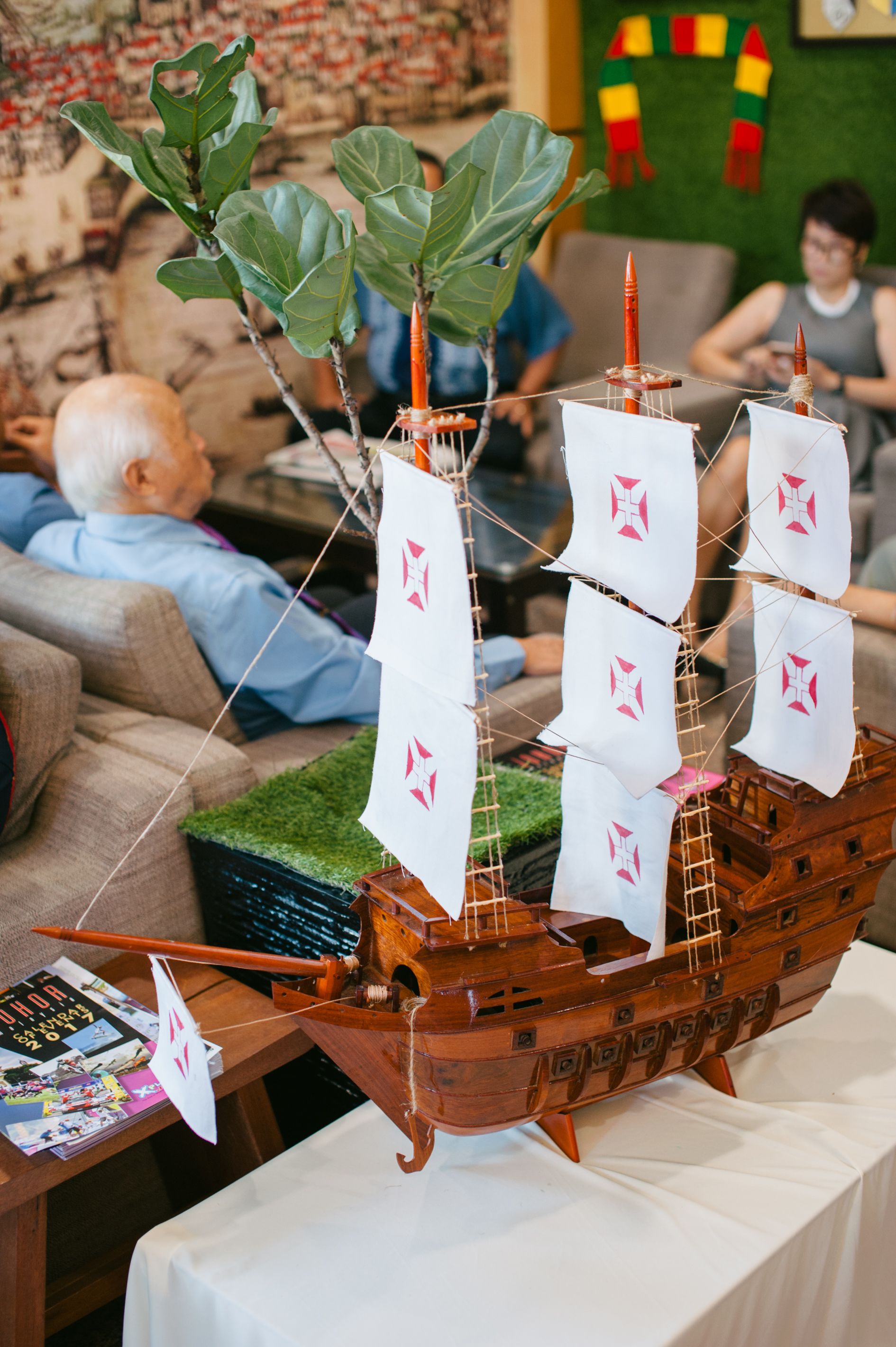 Un modelo de barco sobre una mesa con una revista y una planta verde al lado.
