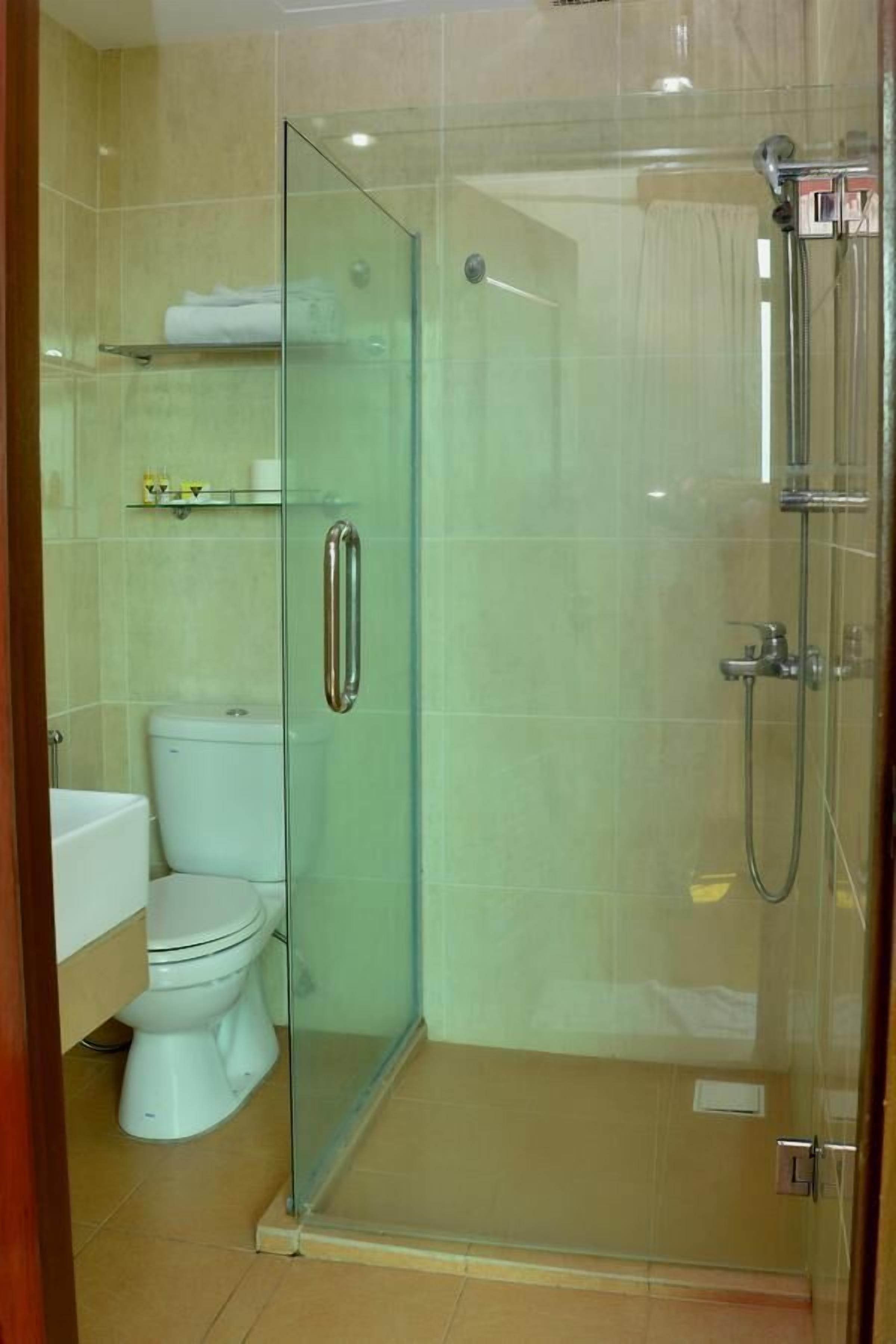 Cabina de ducha con paredes de vidrio, un inodoro y un estante superior.