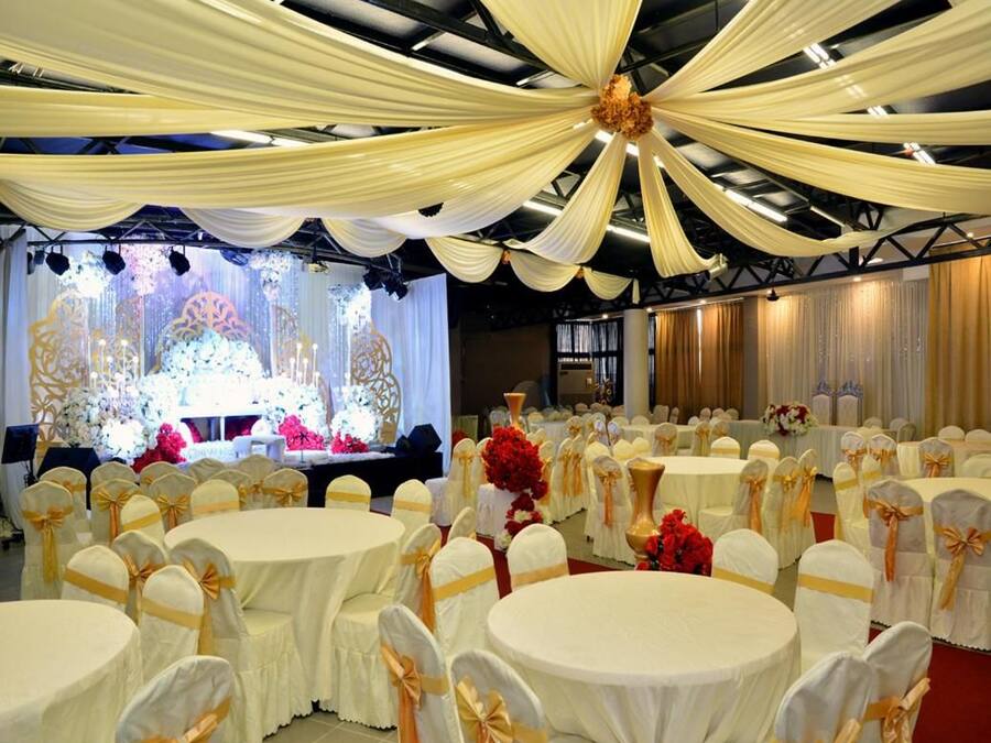 A banquet hall with round tables, chairs with golden sashes, and a stage with floral decorations.