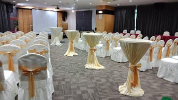 Un salón de conferencias con filas de mesas y sillas blancas, cada una con una cinta dorada.