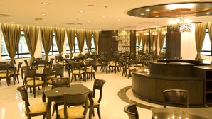 Un vestíbulo de hotel con varias zonas de estar, un mostrador de recepción y amplios ventanales con cortinas.