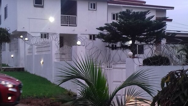 A residential building with a flat roof, multiple windows, and a fenced yard. - HighLander Guest House (Aburi)