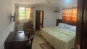 A bedroom with a bed, a desk, a chair, a ceiling fan, and a window with curtains. - HighLander Guest House (Aburi)