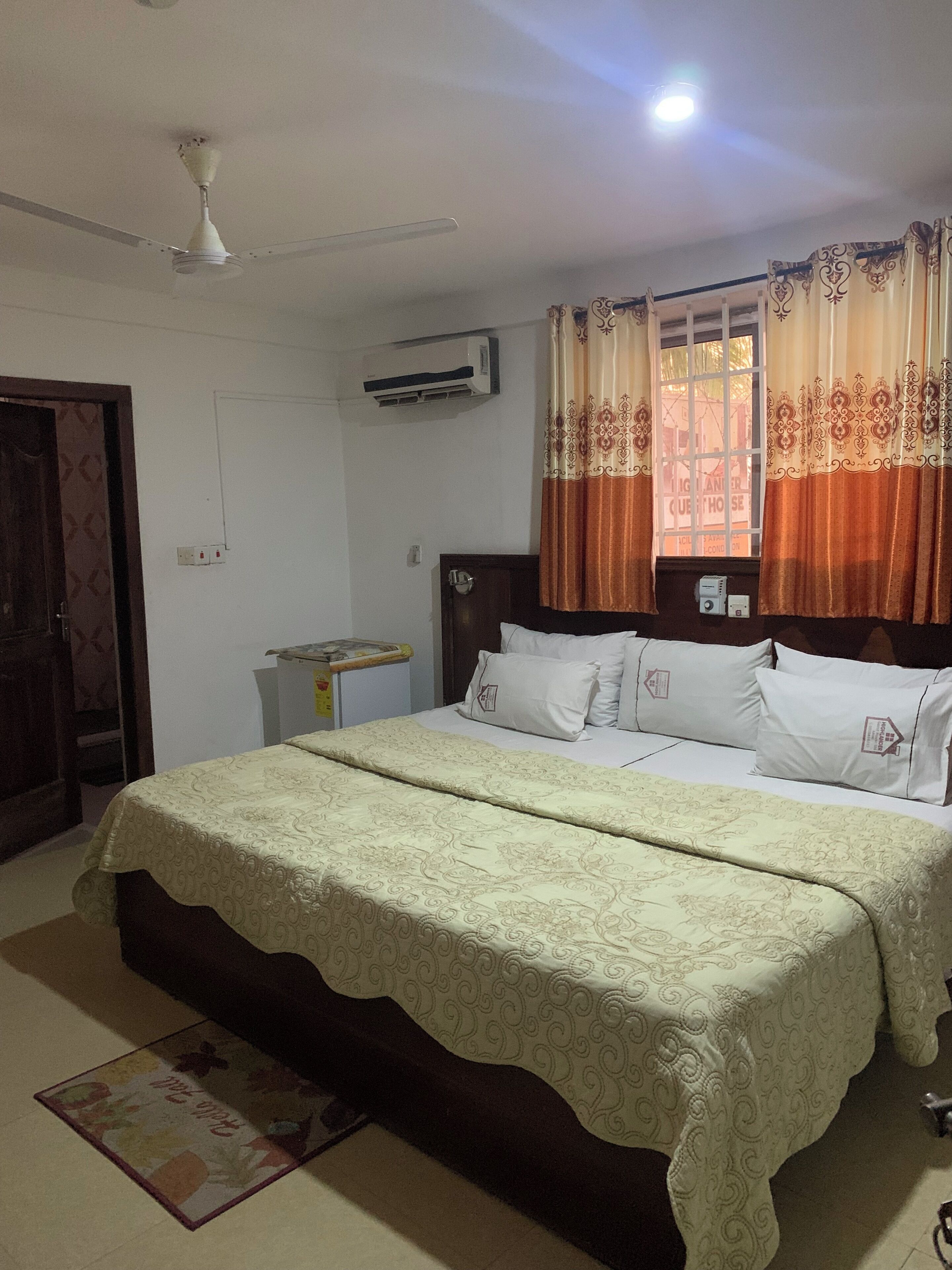 A bedroom with a bed, an air conditioner, a window with curtains, and a ceiling fan.