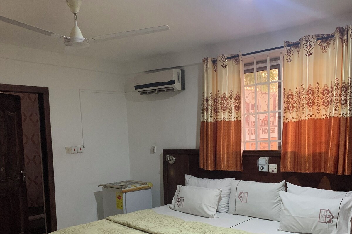 A bedroom with a bed, an air conditioner, a window with curtains, and a ceiling fan.
