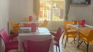 A dining area with a table set for four, surrounded by pink chairs, and a window with metal bars. - HighLander Guest House (Aburi)