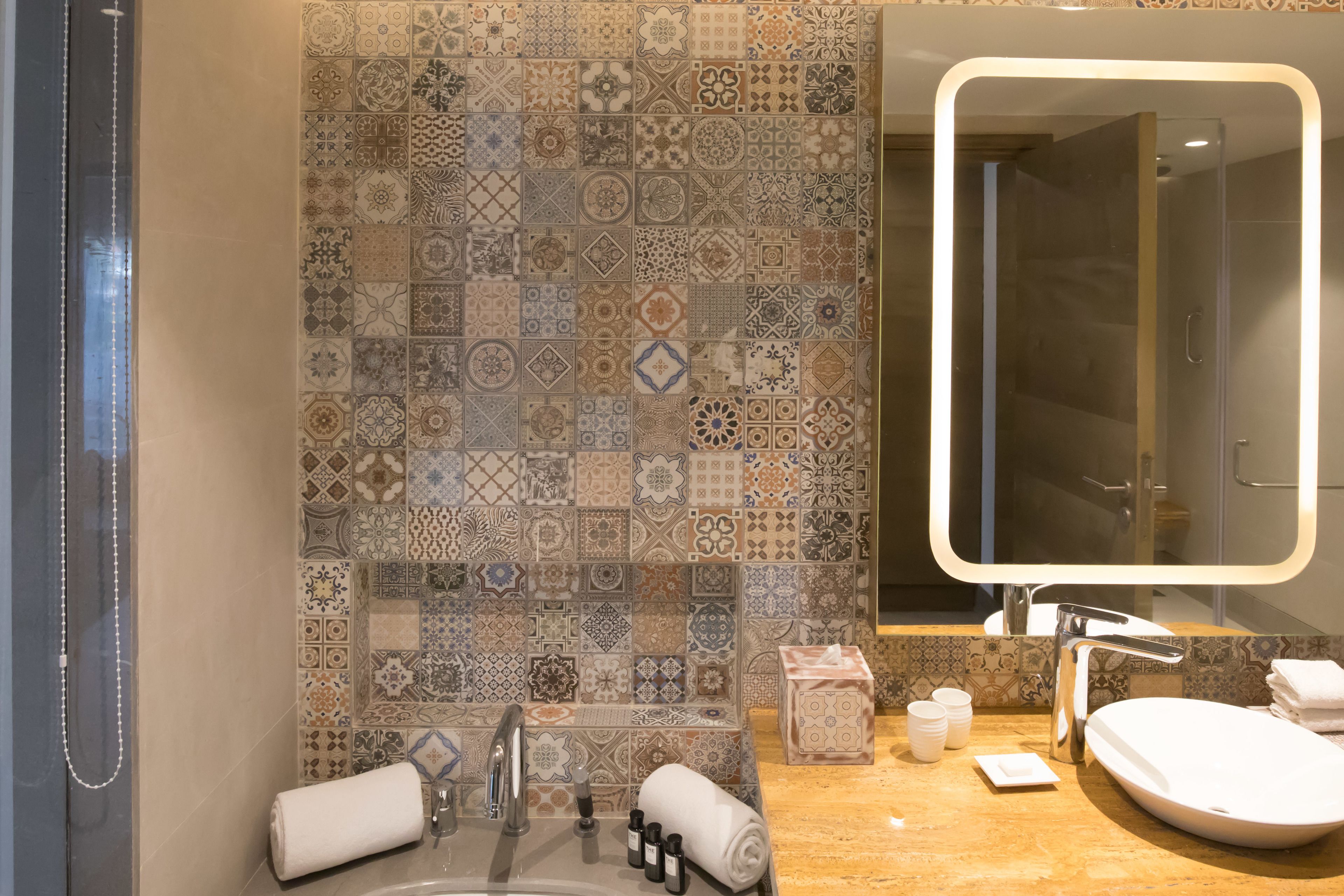Une salle de bain avec un mur recouvert de carreaux derrière le lavabo, un lavabo, un miroir et un espace douche.