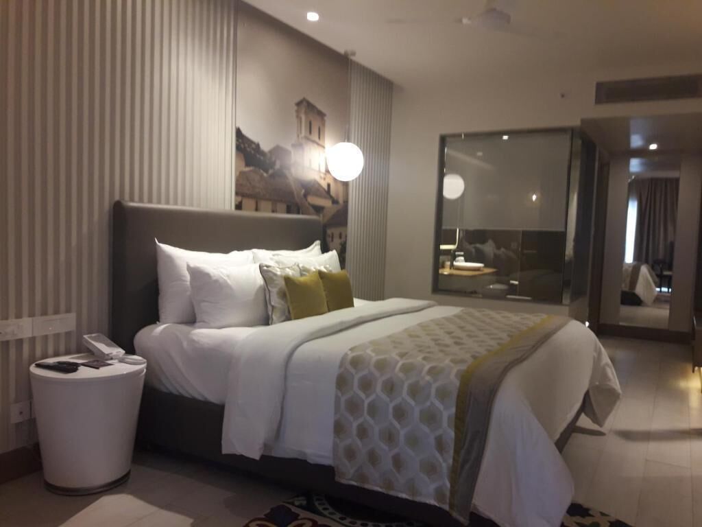 Una habitación de hotel moderna con una cama grande, una mesita de noche con un teléfono, un cesto de basura y un ventanal amplio.