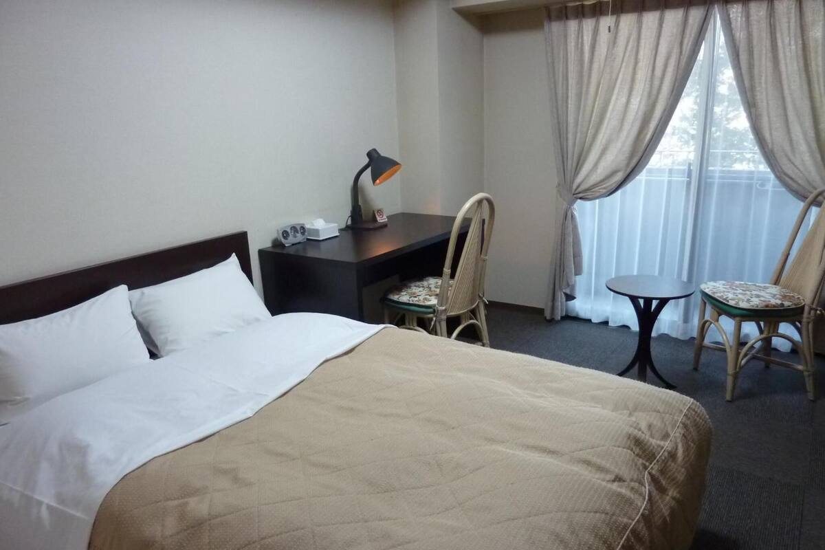 A hotel room with a bed, a desk, a chair, and a small table.