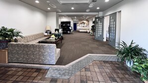A reception area with a sofa, coffee table, and potted plants. There is a reception desk with a computer and a telephone. The floor is carpeted, and the ceiling has recessed lighting. - Sawa Hotel (Fujikawaguchiko)