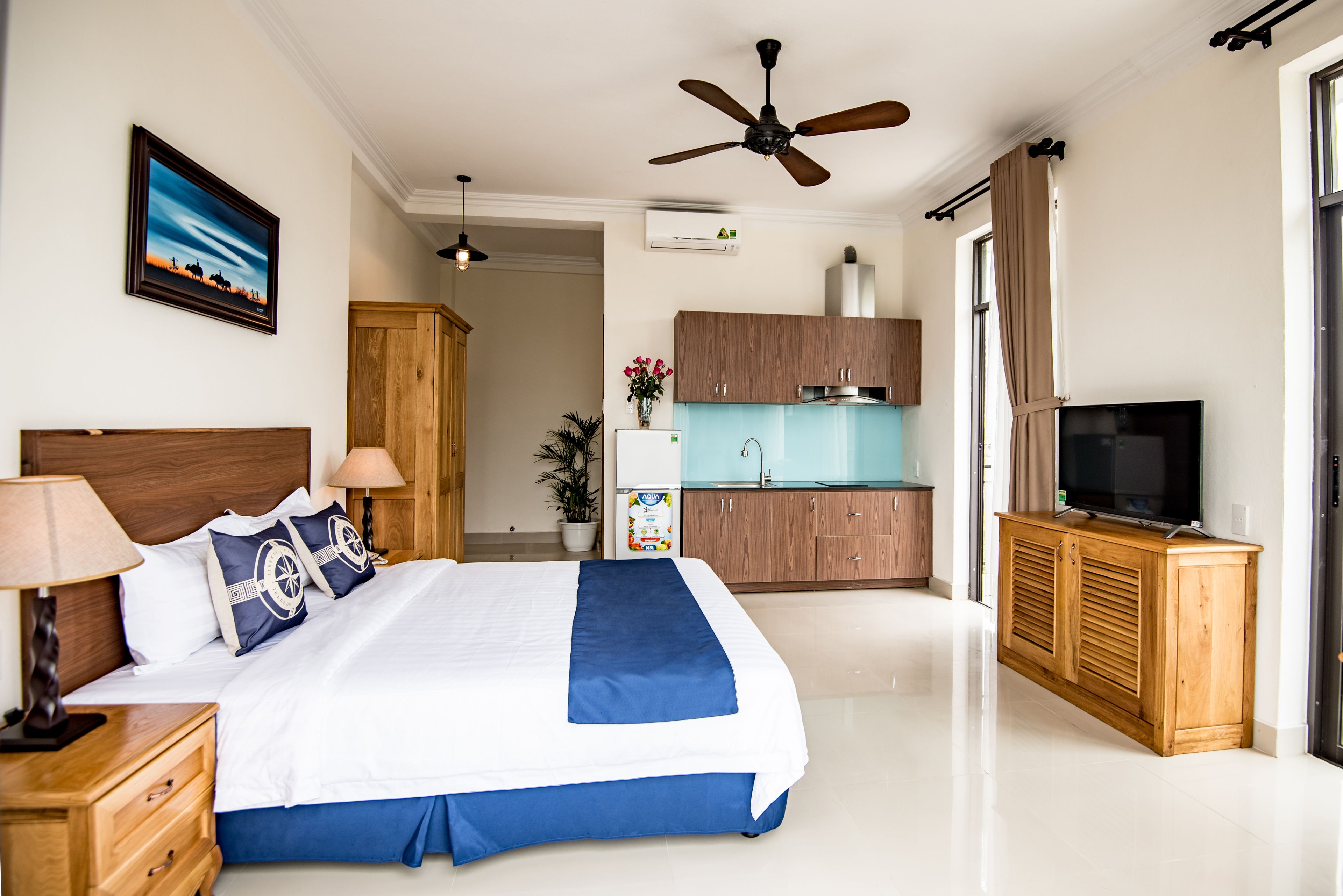 Ein Hotelzimmer mit Bett, Fernseher, Deckenventilator, Küchenzeile und Badezimmer.