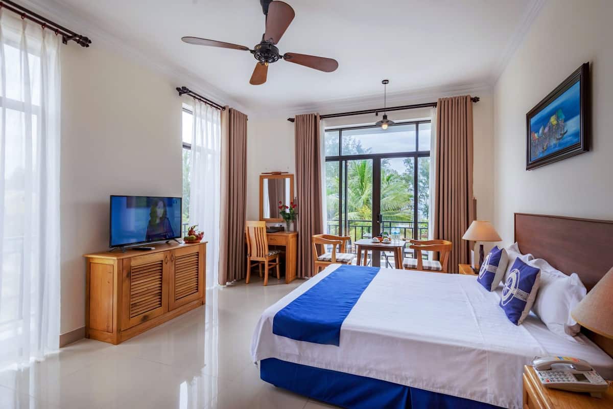 A hotel room with a bed, a desk, a television, and a balcony with a view.