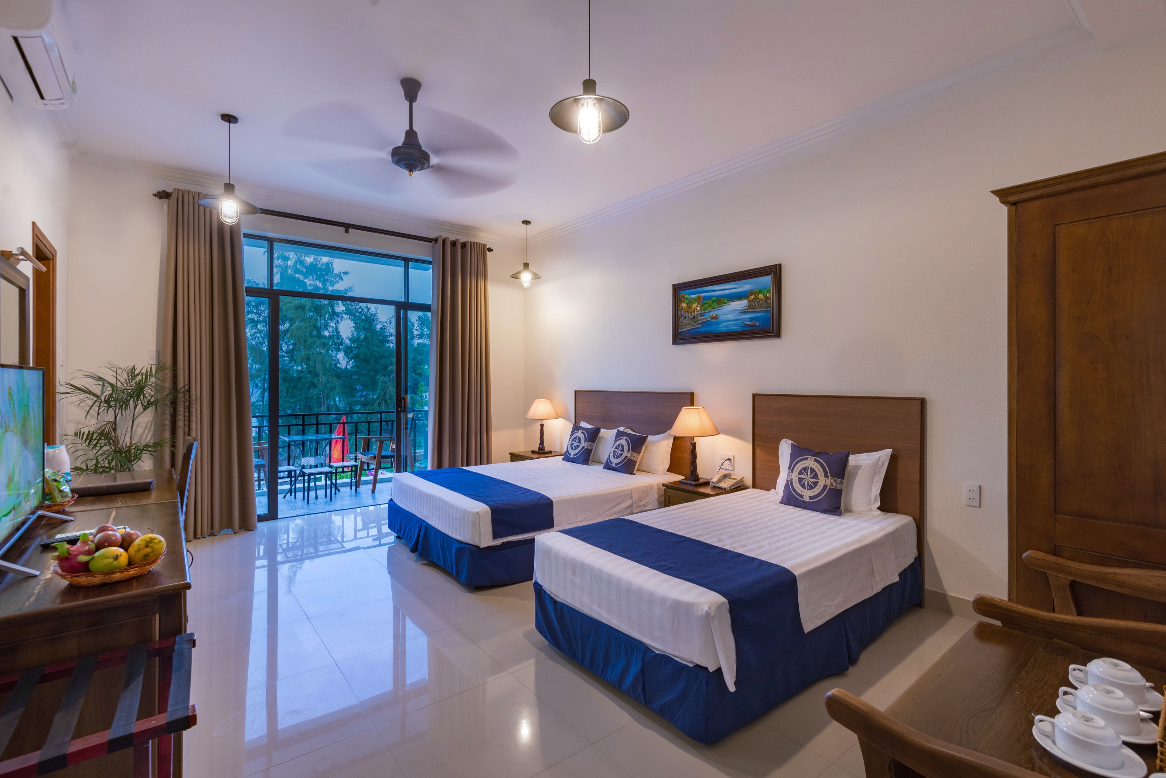 A hotel room with two beds, a balcony with a view, a dining area, and a painting on the wall.