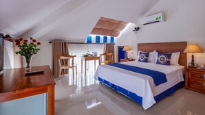 A hotel room with a bed, a desk, a chair, a table, a vase with flowers, and an air conditioning unit. - Santa Sea Villa Hoi An (Da Nang)