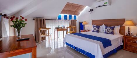 Una habitación de hotel con cama, escritorio, silla, mesa, un jarrón con flores y un equipo de aire acondicionado.