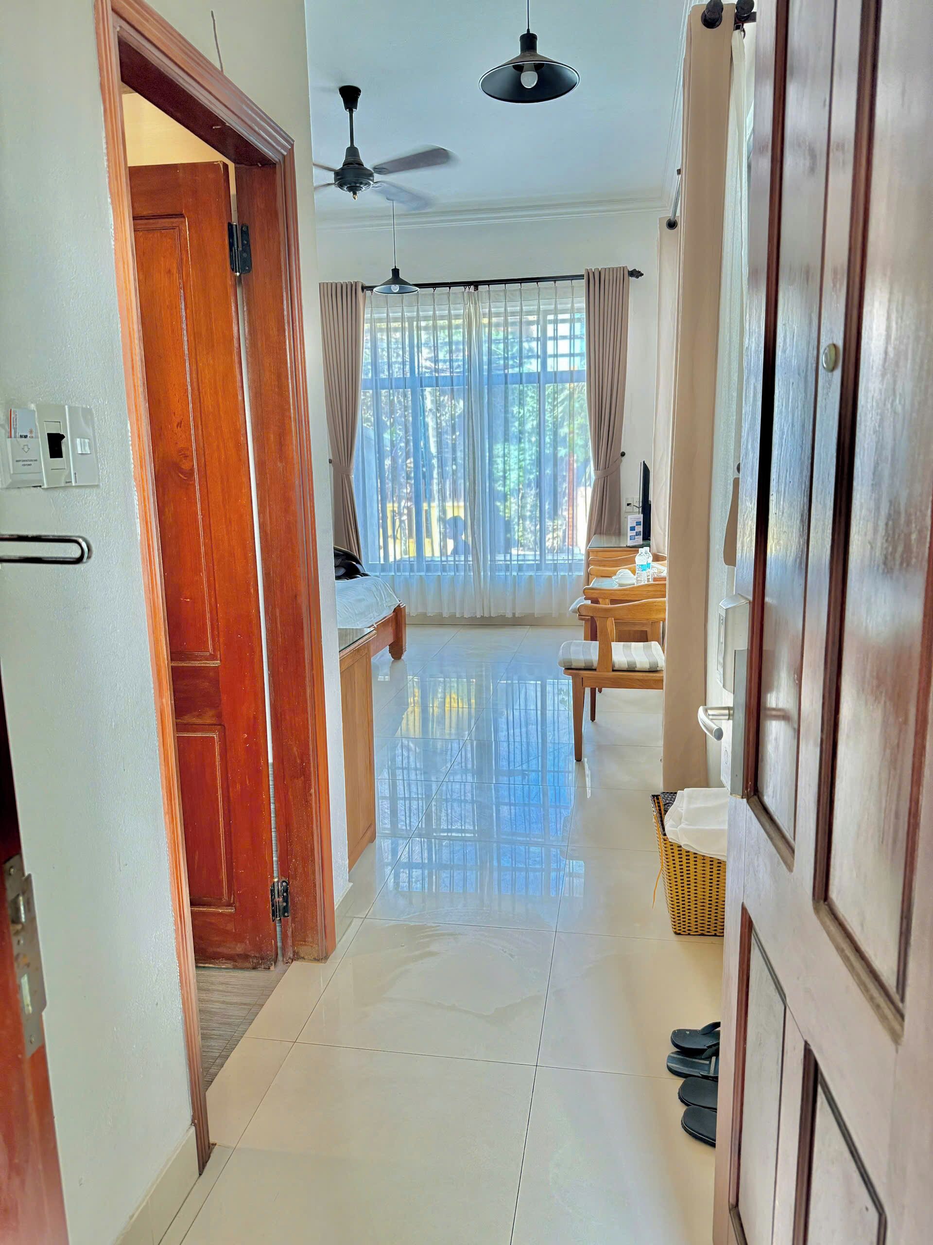A spacious hallway with a wooden door, a ceiling fan, and a large window with curtains.