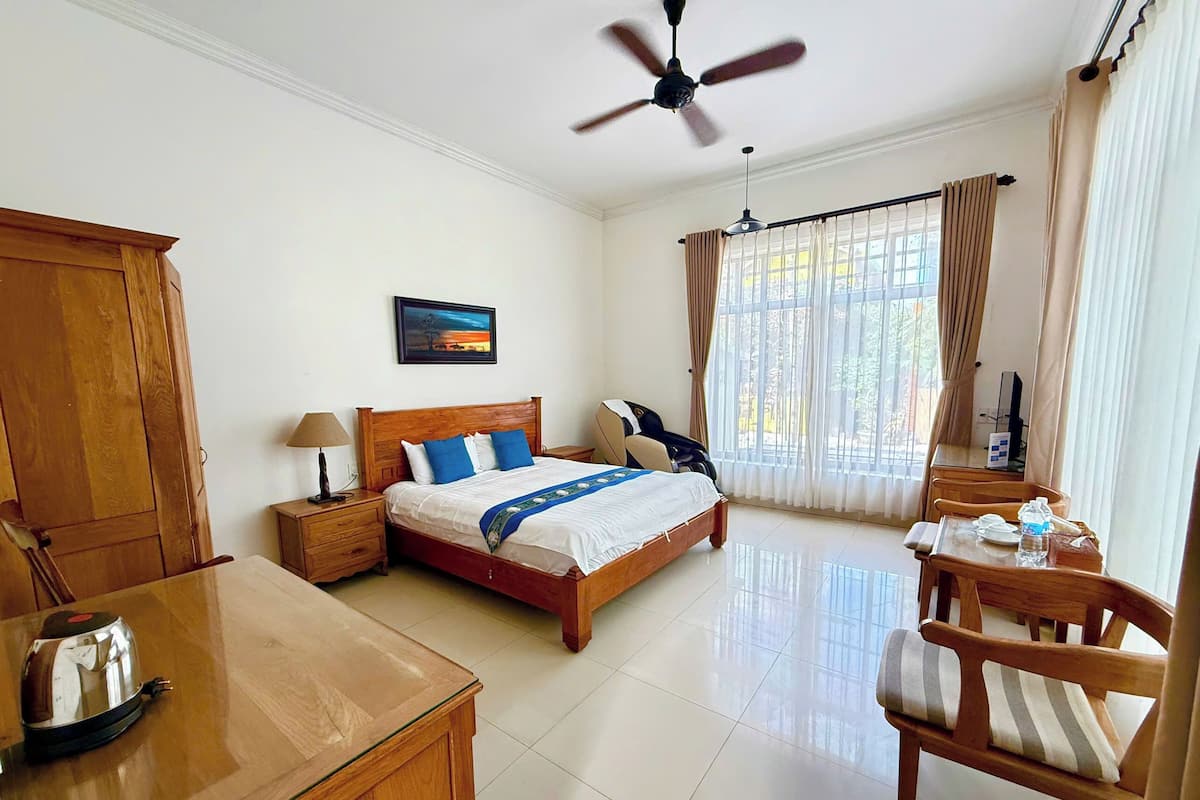 A hotel room with a bed, a desk, a chair, a ceiling fan, and a window with curtains.