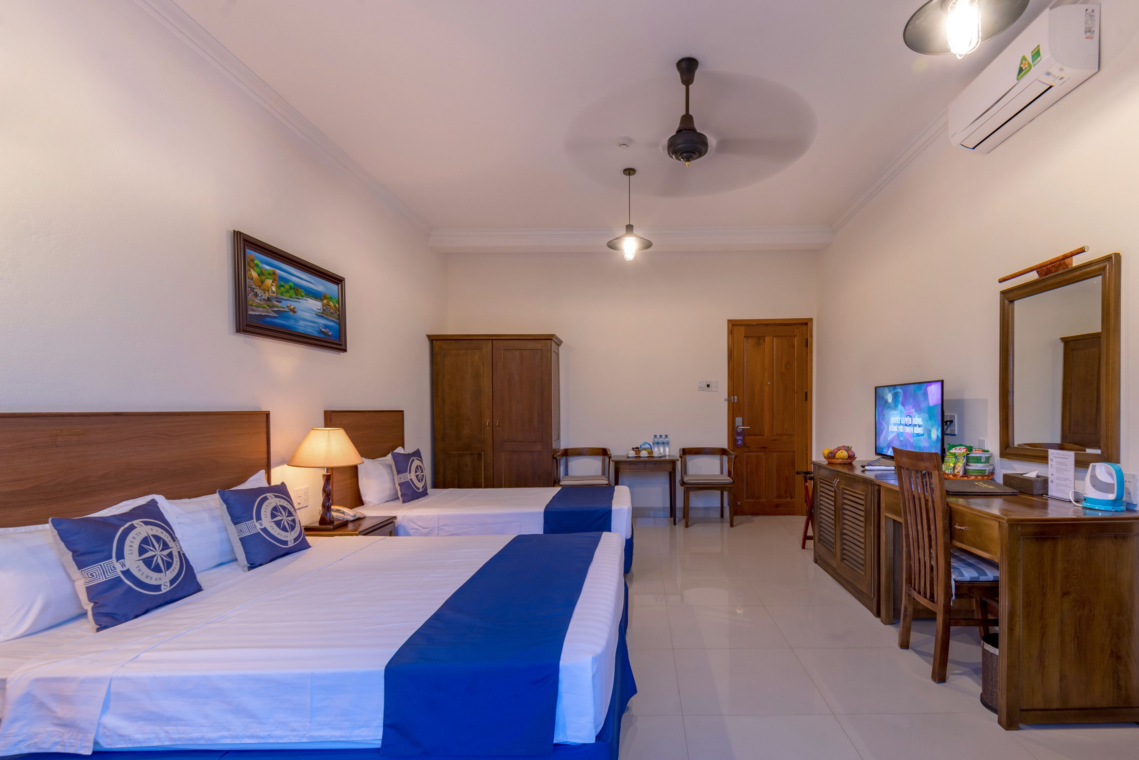 Habitación de hotel con dos camas, un escritorio, una silla, un televisor y un ventilador de techo.