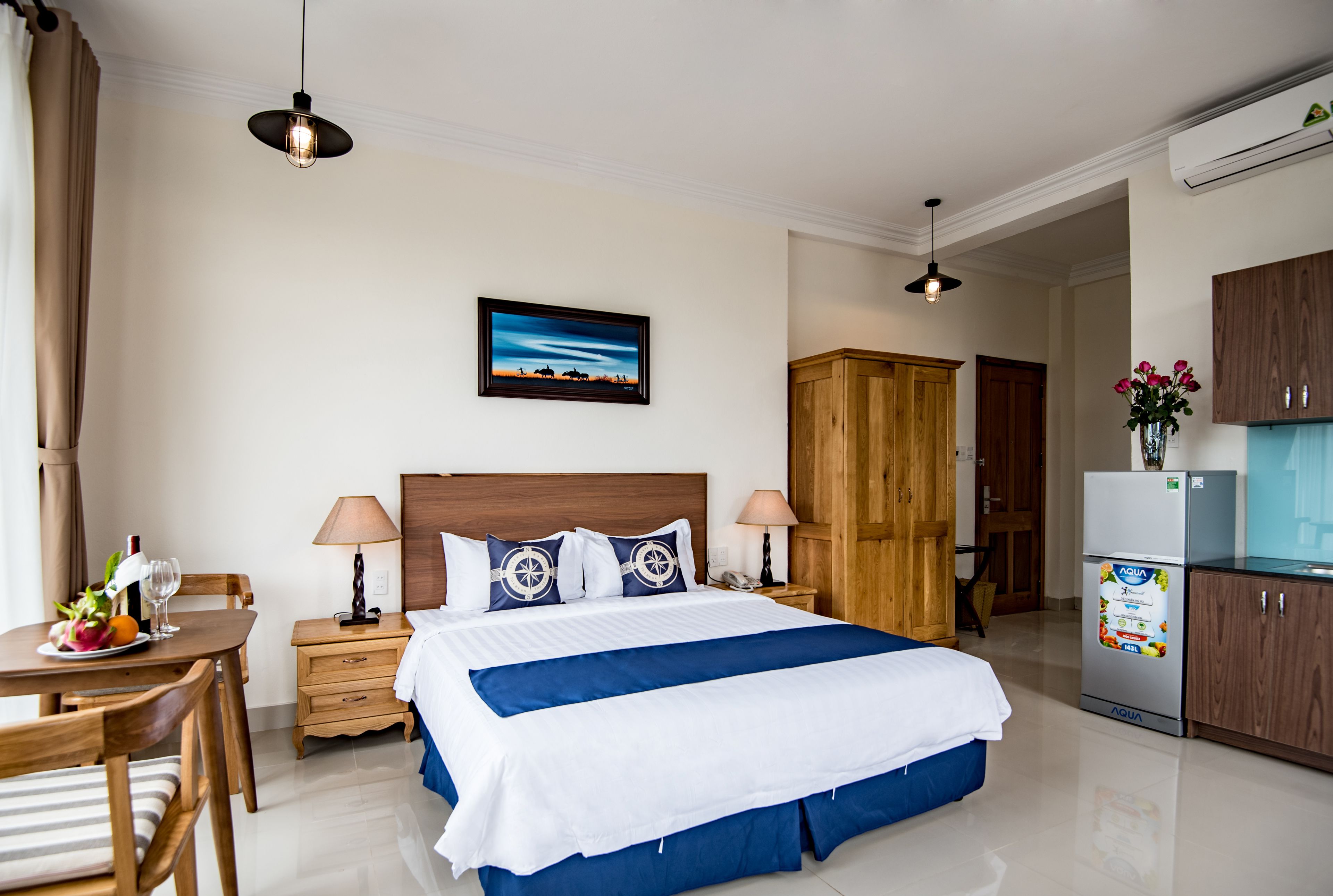 Une chambre d’hôtel comprenant un lit, des tables de chevet, un bureau, une table à manger et un coin cuisine.