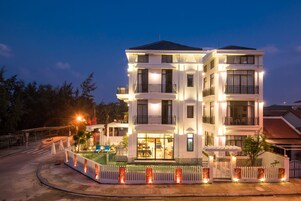 Un hotel de varios pisos con balcones, piscina e iluminación en la fachada.