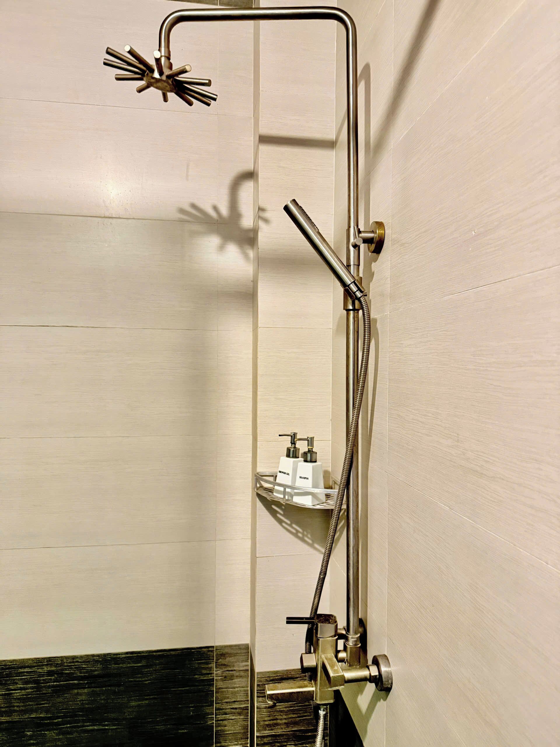 A modern bathroom with a glass shower enclosure, a handheld showerhead, a handheld showerhead with a flexible hose, and a soap dispenser on a shelf.