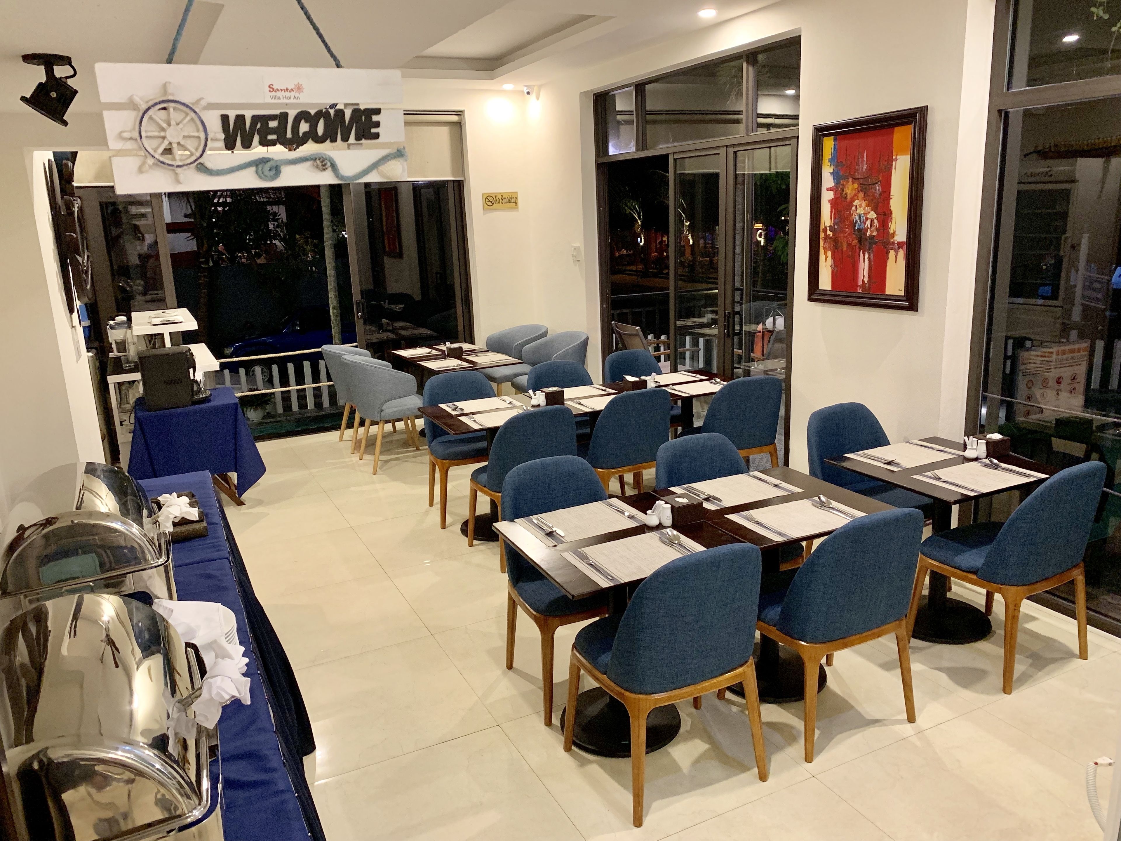A hotel room with a 'Welcome' sign, neatly arranged tables and chairs, and a view through the window.