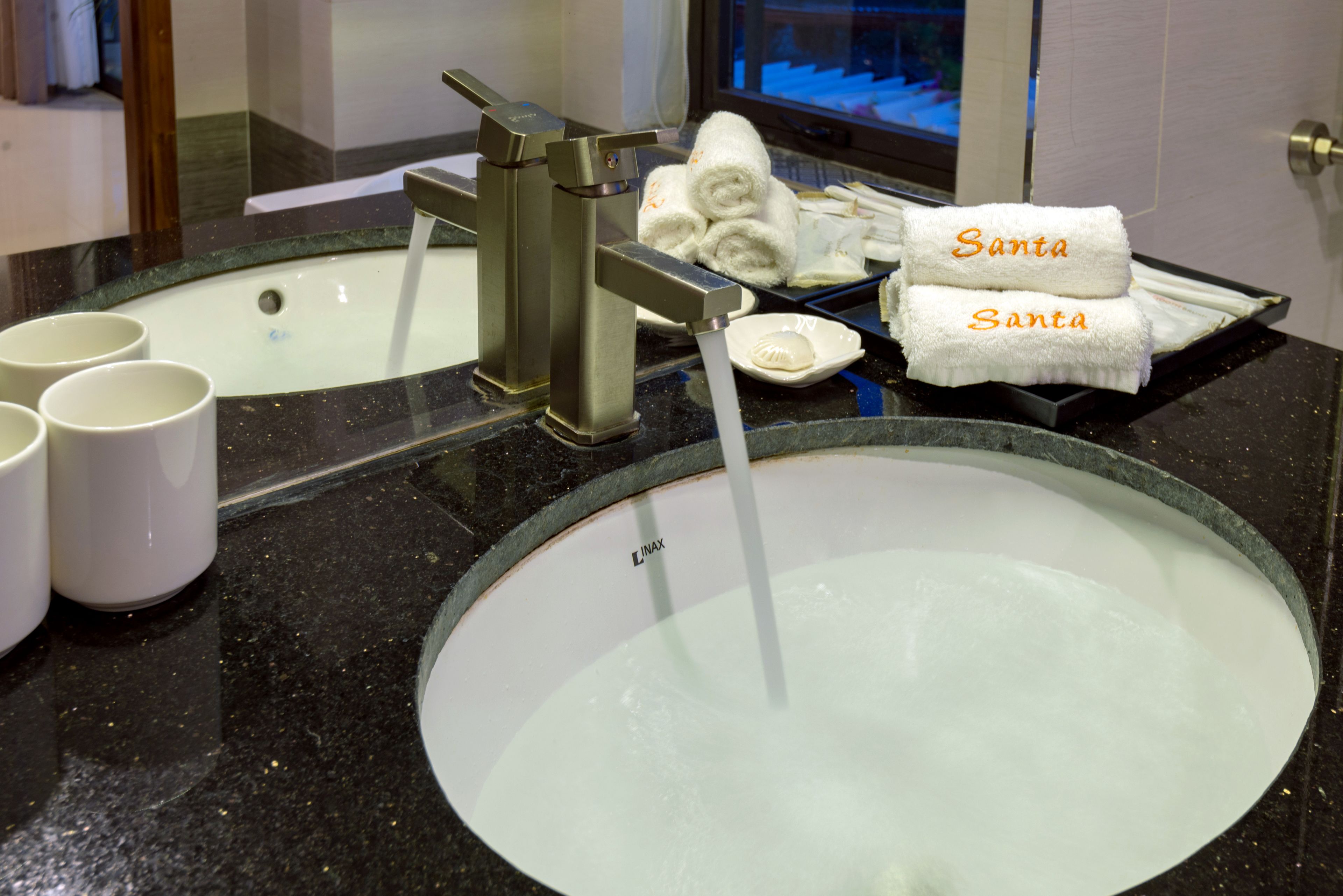 A bathroom sink with running water, a mirror, and a tray with towels labeled "Santa".