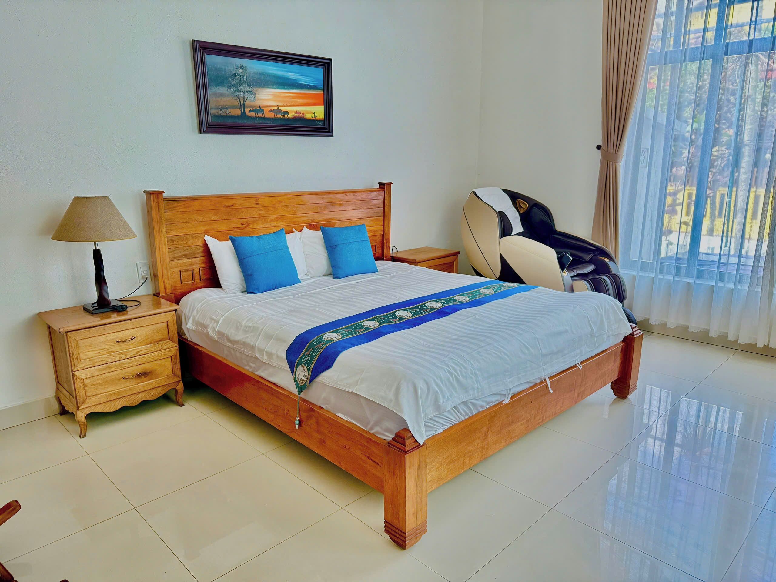 A neatly made bed with a wooden headboard, a bedside table with a lamp, and a massage chair.