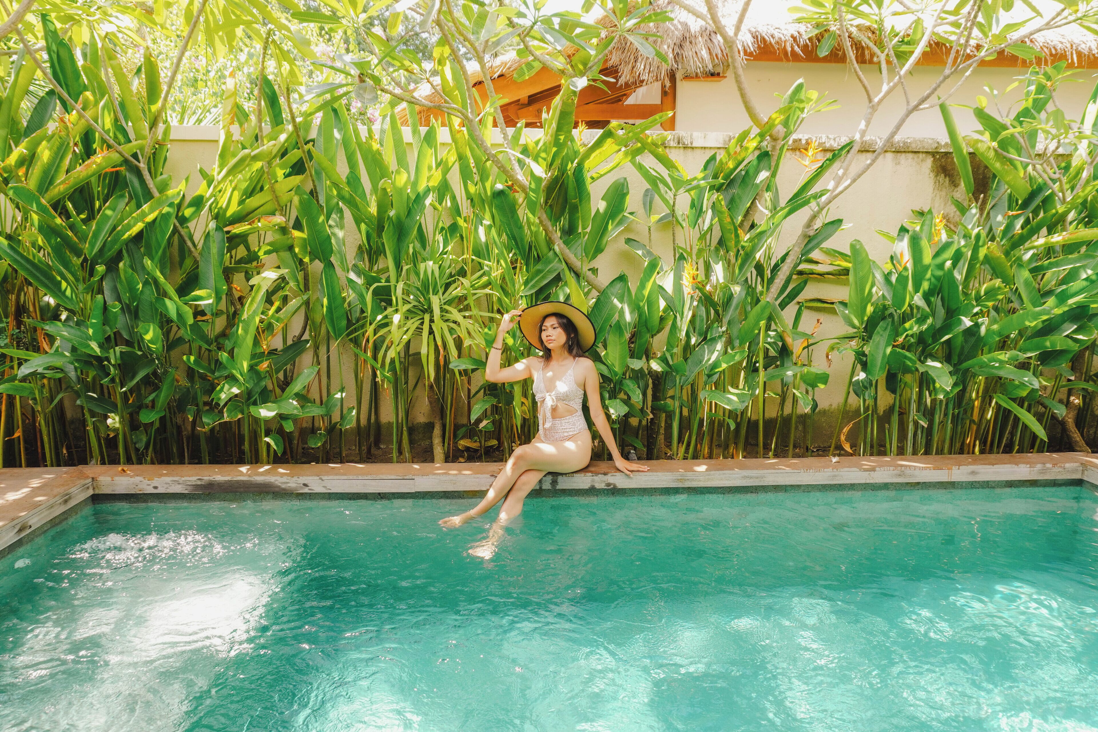 A person sitting by a pool surrounded by lush greenery.