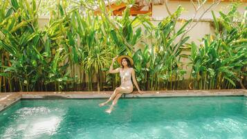 A person sitting by a pool surrounded by lush greenery.