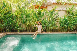 Uma pessoa sentada à beira de uma piscina, cercada por vegetação exuberante.